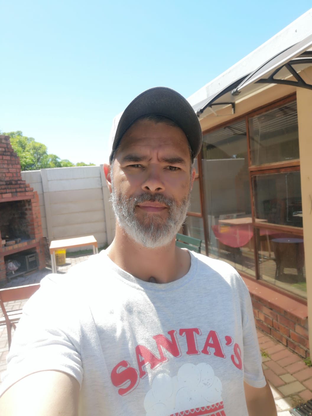 Kevin Vermaak taking a selfie in his backyard. There is a fireplace and a beautiful deck in the background